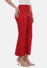 Pantaloni rossi a campana realizzati in tessuto liscio, con vita aderente e tasche frontali, abbinati a scarpe con tacco nudo.