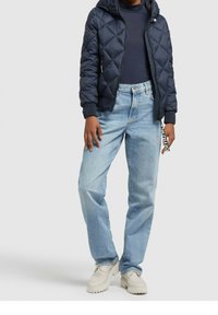 Chaqueta acolchada navy con capucha, combinada con pantalones vaqueros de pierna recta en azul claro y zapatos blancos con suelas estriadas. Lleva un llavero adjunto.
