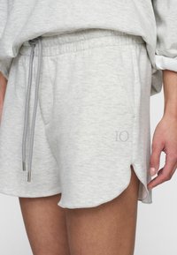 Pantaloni corti in cotone grigio chiaro con vita elasticizzata, dettagli con cordino e fessure laterali. Presentano un piccolo logo '10' in grigio chiaro.