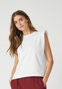 White sleeveless t-shirt made from soft cotton, featuring a round neckline and dropped shoulder design, with a relaxed fit and smooth texture.