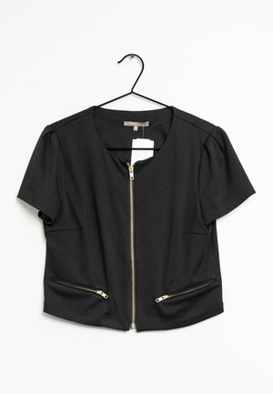 Schwarze Kurzarmjacke mit vorderem Goldreißverschluss und zwei Reißverschlusstaschen, aufgehängt an einem schwarzen Kleiderbügel mit sichtbaren Etiketten.