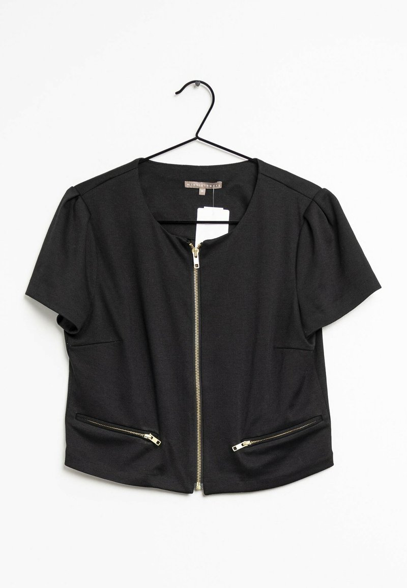 Veste noire à manches courtes avec fermeture éclair dorée à l'avant et deux poches zippées, suspendue sur un cintre noir avec les étiquettes visibles.