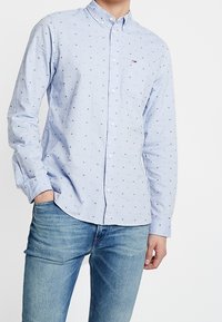Lichtblauwe langemouwen overhemd met kleine marineblauwe stippen, met knopjeskraag, één borstzak en zachte stofstructuur. Gecombineerd met lichtblauwe jeans.
