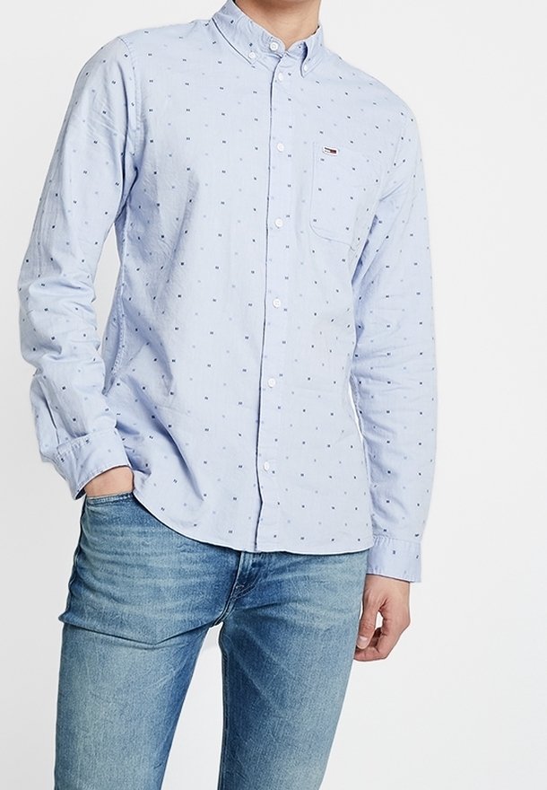 Lichtblauwe langemouwen overhemd met kleine marineblauwe stippen, met knopjeskraag, één borstzak en zachte stofstructuur. Gecombineerd met lichtblauwe jeans.