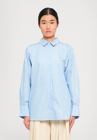 Button-up shirt in light blue with white vertical stripes, featuring a collar, long sleeves, and a chest pocket. Soft texture.