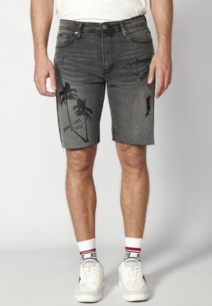 Shorts din denim gri cu tiv despicat, având grafica arborescentelor negre și text. Purtați cu adidași albi și șosete medii.