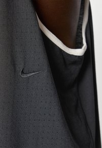 Crna tekstilna majica bez rukava s suptilnim točkastim uzorkom, kontrastnim bijelim izrezom na vratu i ušivenim Nike logoom s lijeve strane.