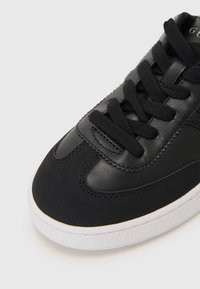 Svart sneaker med lær overdel og teksturerte detaljer, rund tå, flate lisser og hvit gummisåle.