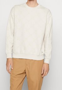 Sweat-shirt beige clair avec motif texturé, col rond, poignets et ourlet côtelés. Associé à un pantalon marron clair.