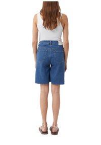 Jeansowe szorty o prostym kroju, z postrzępionym dołem i pięcioma kieszeniami. Pas jest wysoki, a materiał ma średni niebieski kolor z akcentami w postaci przeszyć.