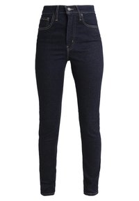 Jeans ajustados de tiro alto de color azul oscuro, hechos de denim, con cremallera, bolsillos frontales y costuras de contraste a lo largo de las costuras.