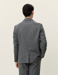 Γκρι σακάκι από ριγέ ύφασμα με μία σχισμή στο πίσω μέρος, διαθέτει γιακά με εγκοπή και δομημένους ώμους. Το ύφασμα φαίνεται υφασμένο.