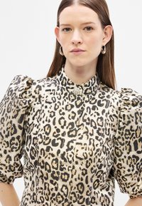 Bluzka w panterkę w kolorach złotym i czarnym, z bufiastymi rękawami i wysokim kołnierzem z ozdobnym guzikiem. Tkanina o fakturze z kontrastującym wzorem.