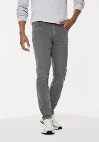 Szare dżinsy slim fit o gładkiej fakturze, z przednimi kieszeniami i klasycznym wzornictwem. W komplecie z białymi butami sportowymi.