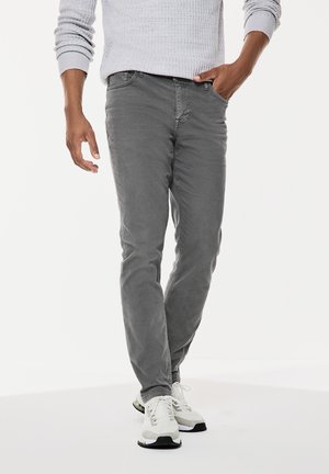 Graue Slim-Fit-Jeans mit glatter Textur, ausgestattet mit Fronttaschen und klassischem Design. Kombiniert mit weißen Sportschuhen.