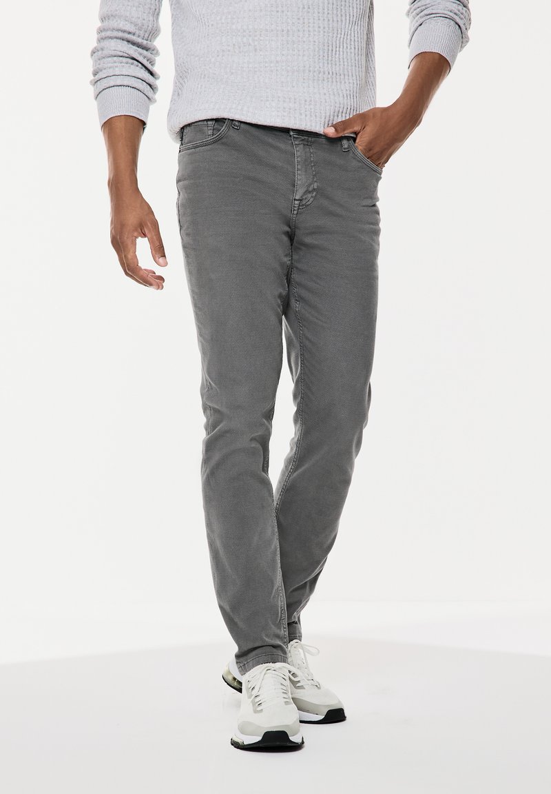 Szare dżinsy slim fit o gładkiej fakturze, z przednimi kieszeniami i klasycznym wzornictwem. W komplecie z białymi butami sportowymi.