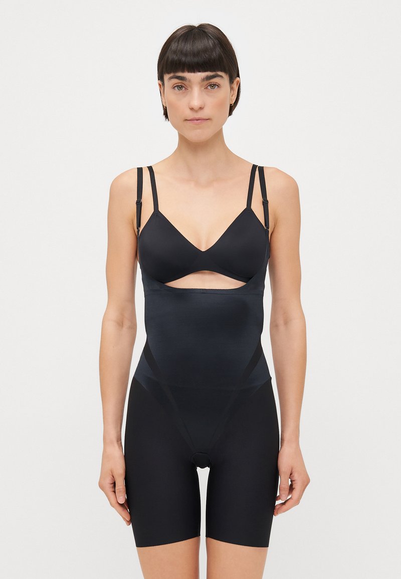 Black shapewear with cutout design, featuring a smooth texture, adjustable straps, and a mid-thigh length. Made from stretchy, lightweight fabric.