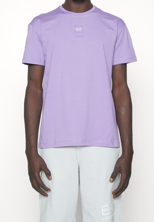 Lila T-Shirt mit kurzen Ärmeln aus Baumwolle mit rundem Ausschnitt. Verfügt über ein kleines EA7-Logo-Label auf der Brust. Glatte Textur und lockere Passform.