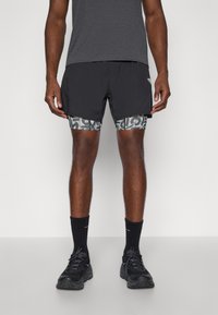 Μαύρες αθλητικές βερμούδες με σχέδιο στη εσωτερική επένδυση, συνδυασμένες με ένα γκρι κοντομάνικο μπλουζάκι και μαύρα αθλητικά παπούτσια. Μαύρες κάλτσες crew.