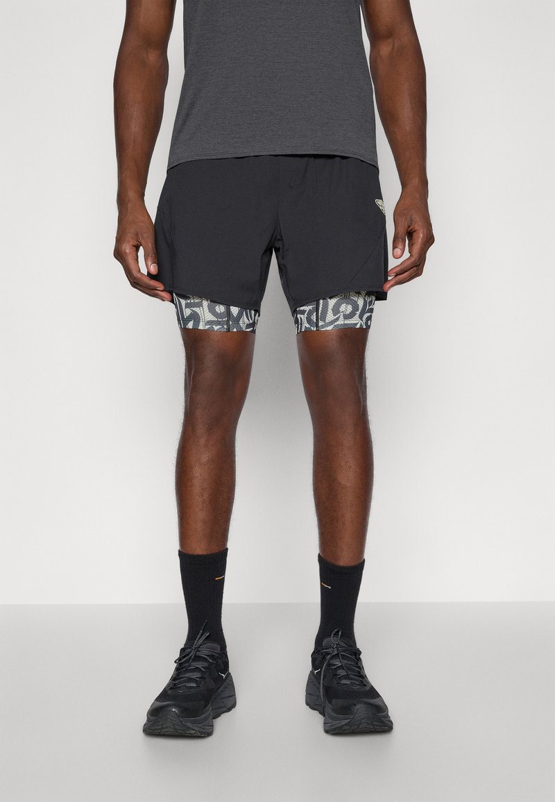 Μαύρες αθλητικές βερμούδες με σχέδιο στη εσωτερική επένδυση, συνδυασμένες με ένα γκρι κοντομάνικο μπλουζάκι και μαύρα αθλητικά παπούτσια. Μαύρες κάλτσες crew.