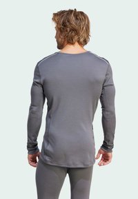 Chemise grise à manches longues avec un col rond, ajustée, et texture lisse. Présente des coutures contrastantes le long des épaules et des poignets.