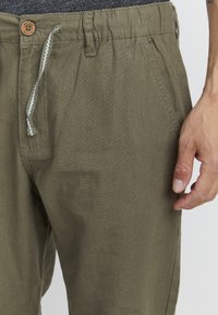 Olijfgroene linnenblendbroek met een elastische tailleband, trekkoord en houten knoop; voorzien van zijzakken en nette stiksels.