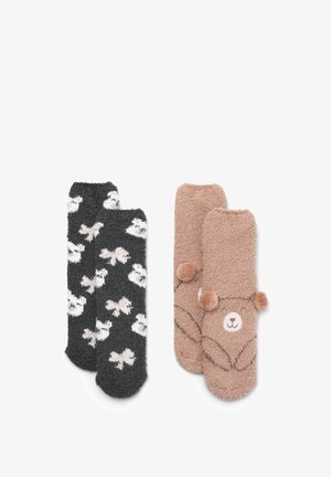 Due paia di calzini morbidi: uno nero con motivi di animali bianchi, l'altro marrone chiaro con un design di orso e pompon sui lati.
