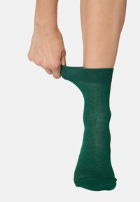 Calzino di cotone verde tirato con una mano, caratterizzato da una superficie a coste e un design di lunghezza standard.