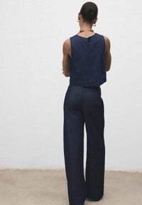 Top court en denim foncé avec un détail en fente au dos, associé à un pantalon large en denim foncé, tous deux présentant un design épuré et minimaliste.