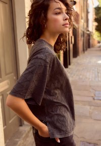T-shirt a maniche corte di colore grigio scuro con dettagli a motivo diamante. Materiale morbido con una vestibilità rilassata, abbinato a pantaloni scuri.