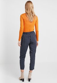 Pomarańczowa bluzka z długim rękawem zestawiona z granatowymi spodniami w paski. Spodnie mają elastyczny pas i zwężane kostki. Beżowe botki za kostkę.