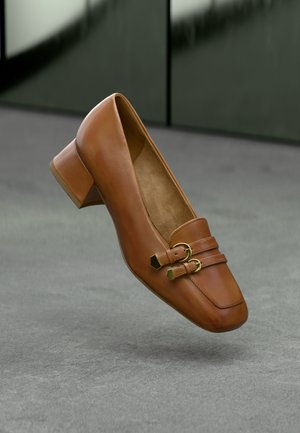 Brauner Leder-High-Heel-Schuh mit quadratischer Zehenpartie, der zwei dekorative Riemen und goldfarbene Hardware-Akzente aufweist. Glatte Textur, minimalistisches Design.