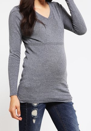 Graues V-Ausschnitt Langarmshirt aus weichem Material, figurbetonte Passform mit einem dehnbaren Bund, kombiniert mit abgetragenen blauen Jeans. Keine auffälligen Muster oder Akzente.