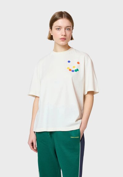 Camiseta de algodón crema con mangas cortas, que presenta un patrón de puntos coloridos en tonos de azul, verde, naranja y amarillo en el pecho.