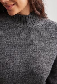 Pull tricoté gris foncé avec un col montant côtelé, présentant une texture douce et une coupe décontractée, avec peu de détails sur le tissu.