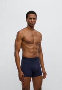 Μπλε ναυτικού χρώματος ανδρικά μποξεράκια από απαλό βαμβάκι με μαύρη ελαστική μέση που διαθέτει χαραγμένα λογότυπα και εφαρμοστή σχεδίαση.