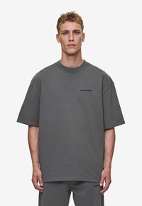 Übergroßes graues T-Shirt aus Baumwolle mit rundem Ausschnitt und kurzen Ärmeln. Dezentes schwarzes Logo auf der Brust. Angenehme Textur.