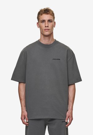 Överstor grå T-shirt i bomull med rund halsringning och korta ärmar. Diskret svart logotyp på bröstet. Slät yta.