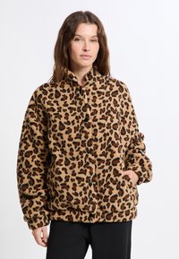 Kurtka w leopardzi wzór z materiału pluszowego; posiada stojący kołnierz, zapięcie na guziki oraz kieszenie z przodu. Paleta kolorów obejmuje beżowy, brązowy i czarny.