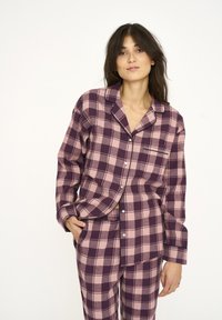 Purple and pink plaid pajama set with long sleeves and matching pants, featuring a button-up shirt and a pocket detail. Soft fabric texture.