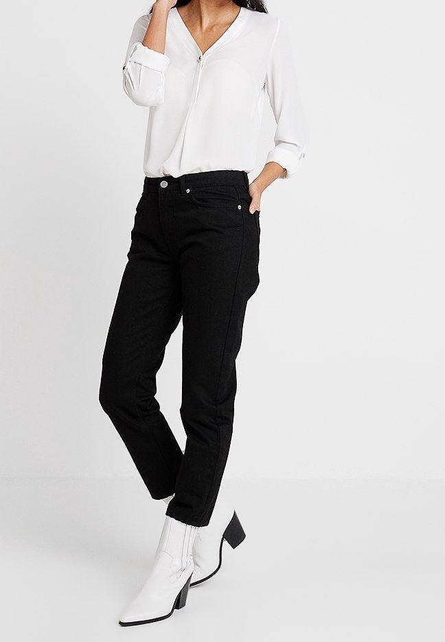 Černé tapered džíny s vysokým pasem, pětikomorový design, denimový materiál, spárované s bílou blůzkou a bílými polobotkami na podpatku.