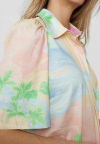 Chemise à manches courtes présentant un design pastel avec des palmiers, des vagues et des formes abstraites. Confectionnée en tissu léger à la texture douce.