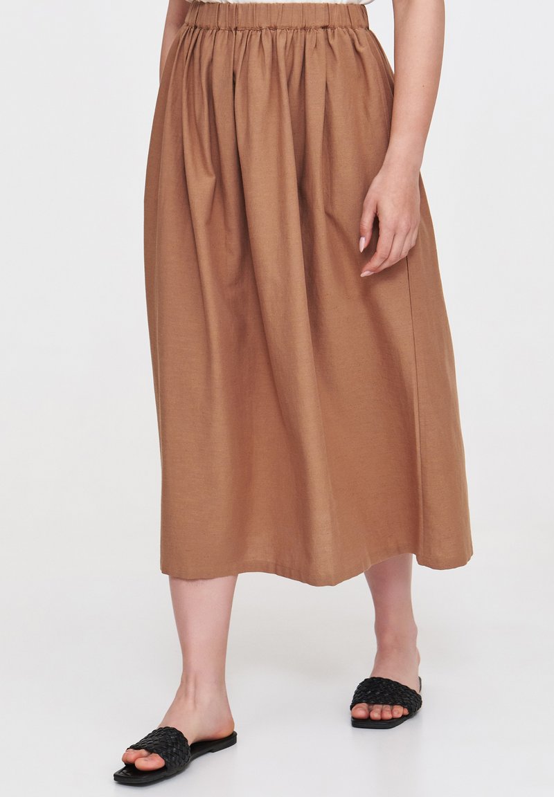 Brąskowa spódnica do kolan z marszczonym elastycznym pasem, wykonana z lekkiego materiału. Połączona z czarnymi plecionymi sandałami-klapkami.