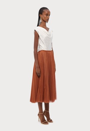 Un top en satin blanc avec un décolleté drapé, associé à une jupe midi en tulle orange. Comprend des talons hauts beiges à lanières et un tissu texturé.