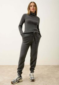 Tummanharmaa ribattu poolopaita yhdistettynä harmaisiin naruhousuihin. Asusteena urheilulliset lenkkarit. Sujuva pinta, rento malli.