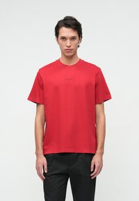 Czerwona bawełniana koszulka z krótkim rękawem i okrągłym dekoltem. Posiada małe logo nadrukowane w okolicy klatki piersiowej. Gładka tekstura, luźny krój.