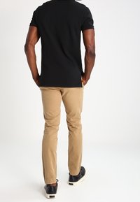 Svart kortärmad polo, beige slim-fit byxor och svarta sneakers med vita sulor. Enkel design, bomullstyg och neutrala färger.