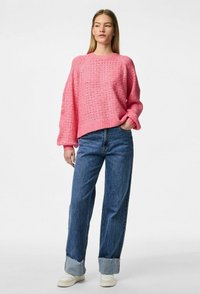 Maglione rosa lavorato a maglia con un motivo testurizzato, maniche larghe e una vestibilità rilassata, abbinato a jeans blu a vita alta e sneakers bianche.