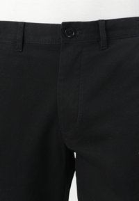 Sorte bomullsbukser med knappelukking, flat front og buede sidelommer. Stoffet har en glatt tekstur med minimale detaljer.