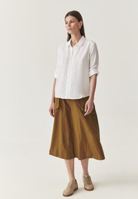 Witte knopsluiting overhemd met opgerolde mouwen, gecombineerd met een knielange mosterdrok en beige veterschoenen. Glad materiaal, comfortabele pasvorm.
